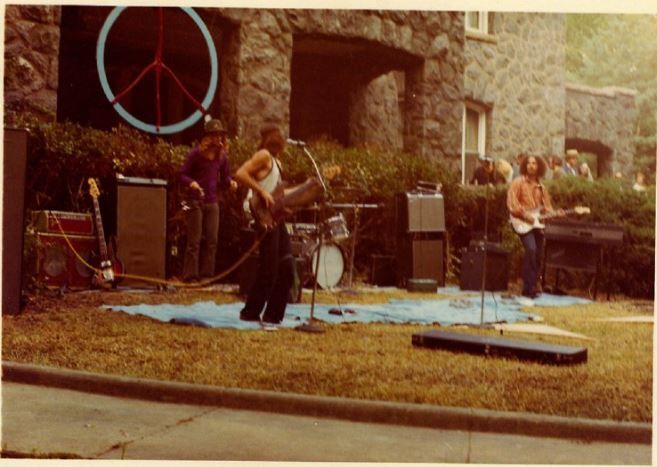 Musicians perform on a scrappy stage in front of the granite mansion